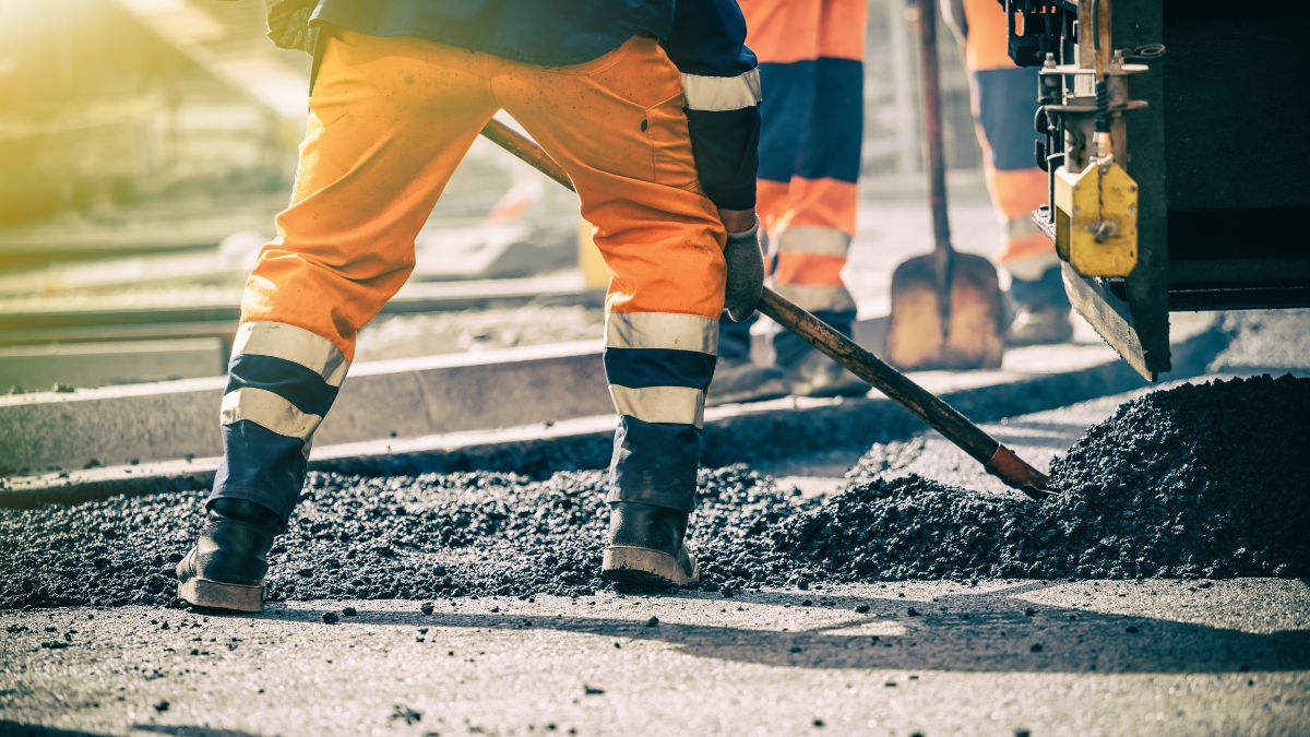 Straßenarbeiter mit Schaufel verteilt Asphalt auf Baustelle in Österreich