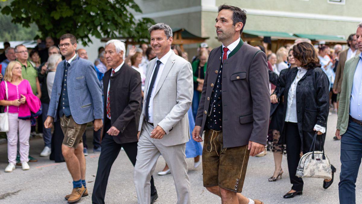 Trachtler und Anzugträger marschieren bei einem Festzug in Österreich.